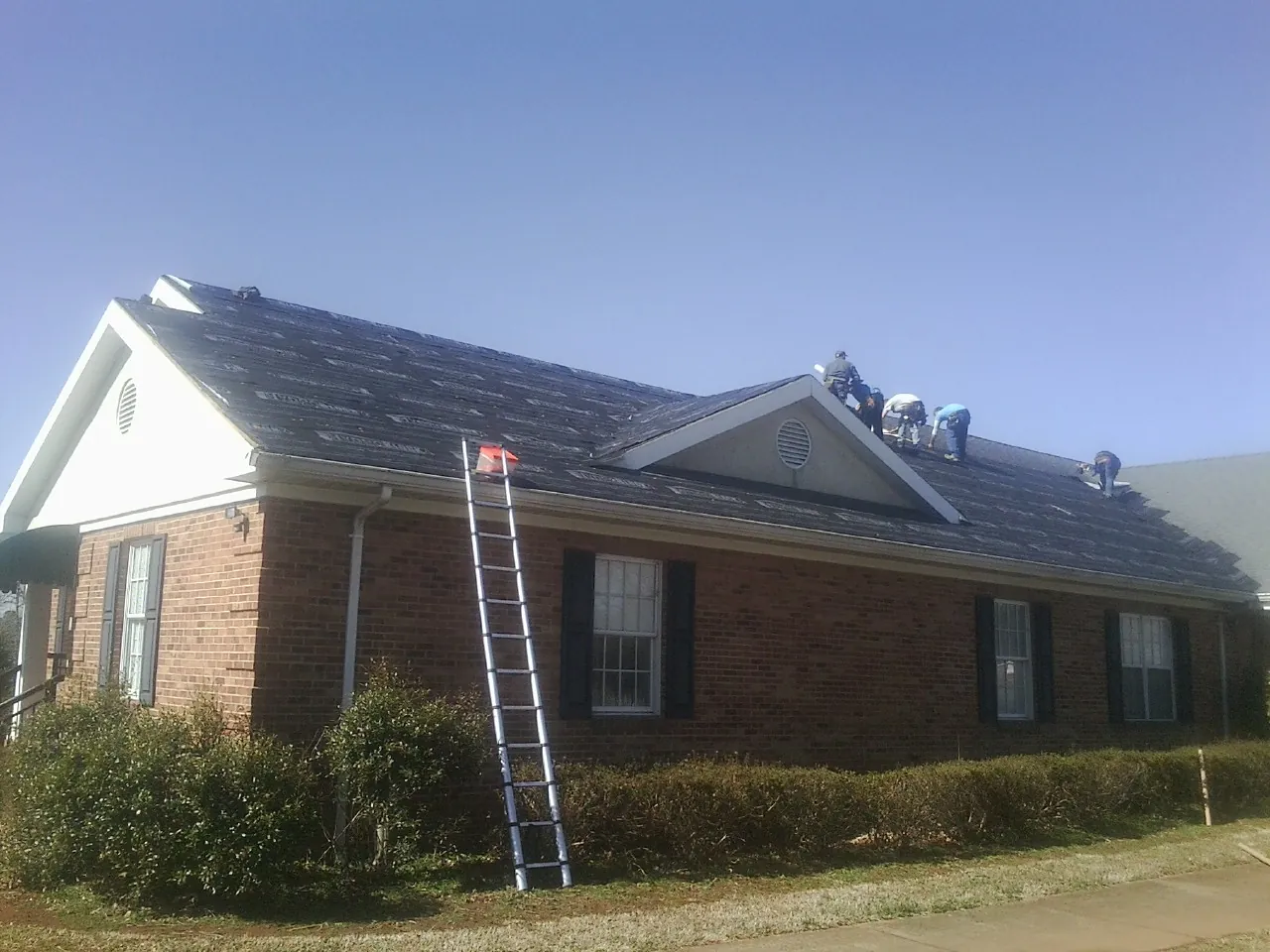 Crew tearing shingles off a brick ranch roof with a ladder set — Metal Roof Repair work by our crew in York